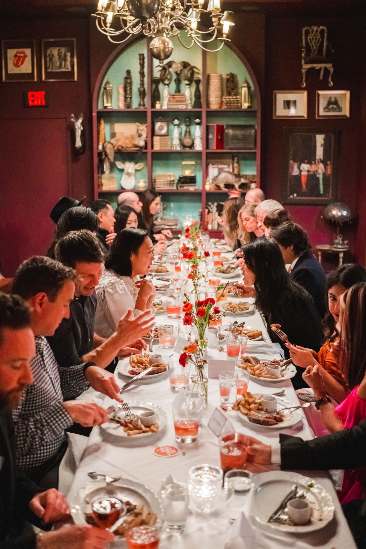 A long supper table running the length of a deep red room, guests down both sides